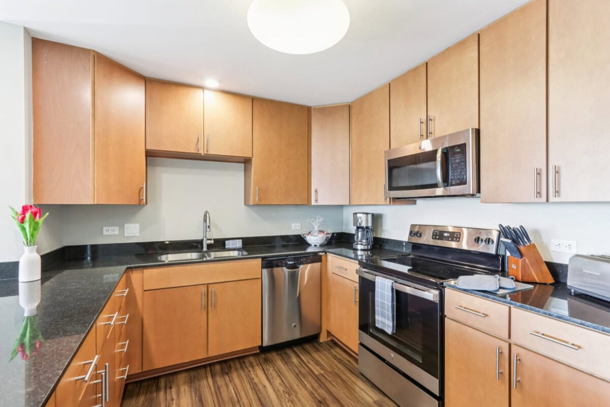 Modern kitchen with light wood cabinets, stainless steel appliances, black granite countertops, and a vase of red tulips on the counter.