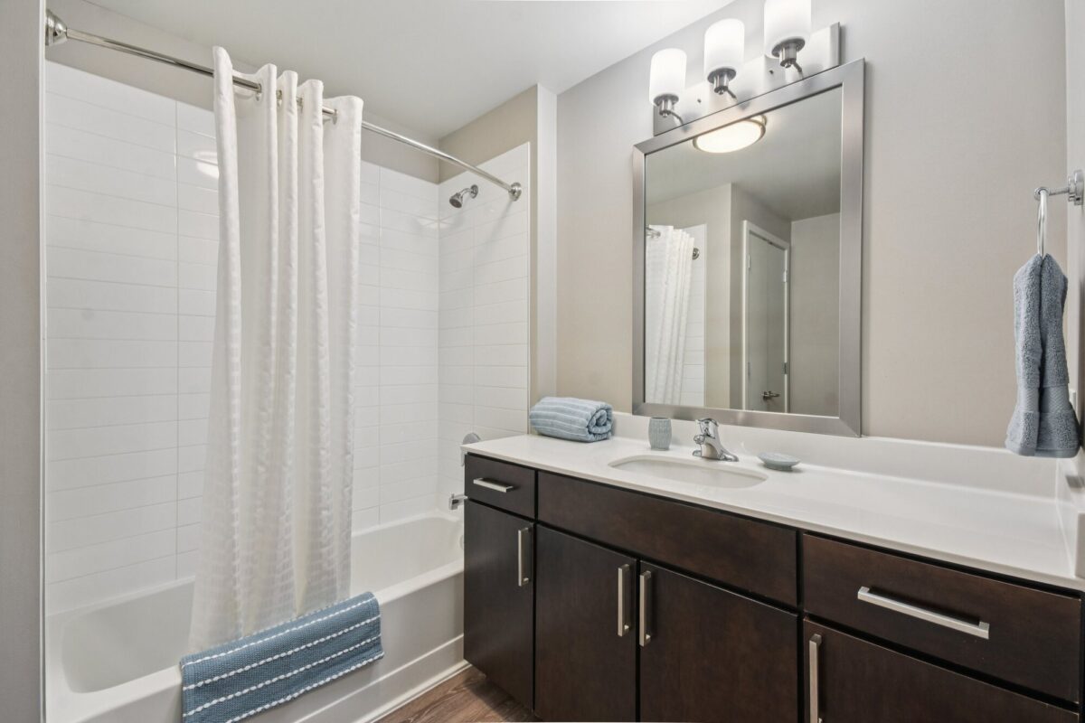 Modern bathroom with a white bathtub and shower, dark wood vanity with double sinks, large mirror, and neatly folded blue towels.