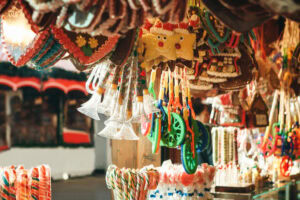 A festive market stall displays colorful sweets, candy canes, gingerbread cookies, toy trumpets, and star-shaped treats, creating a cheerful and vibrant holiday atmosphere.