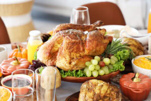 A roasted turkey on a platter with lettuce and grapes, surrounded by side dishes, glassware, and pumpkins on a festive dining table.