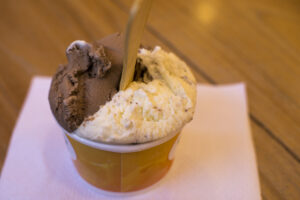 A small cup of chocolate and vanilla ice cream with a wooden spoon, placed on a white napkin on a wooden table.