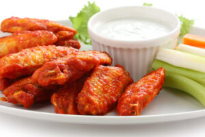 A plate of spicy buffalo chicken wings with celery and carrot sticks, served with a cup of creamy ranch or blue cheese dipping sauce, garnished with a lettuce leaf.