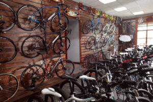 A bicycle shop interior with various bikes hanging on wooden walls and more bikes displayed on the floor. The shop is well-lit, and cycling accessories are visible on shelves and walls.