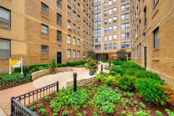 Well-maintained courtyard with landscaped greenery and pathways, surrounded by a multi-story brick apartment building.