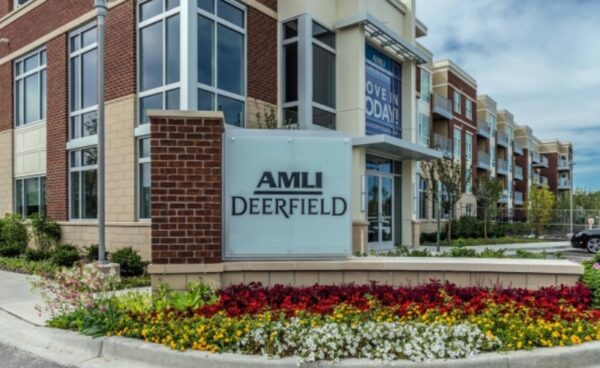 Exterior view of AMLI Deerfield apartment complex with a prominent sign and landscaped flower bed in front.