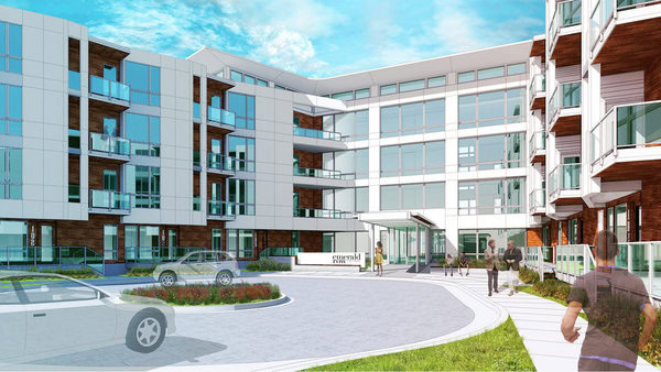 Modern apartment complex with large glass windows, multiple balconies, and a circular driveway with parked cars, people walking along the pathway.
