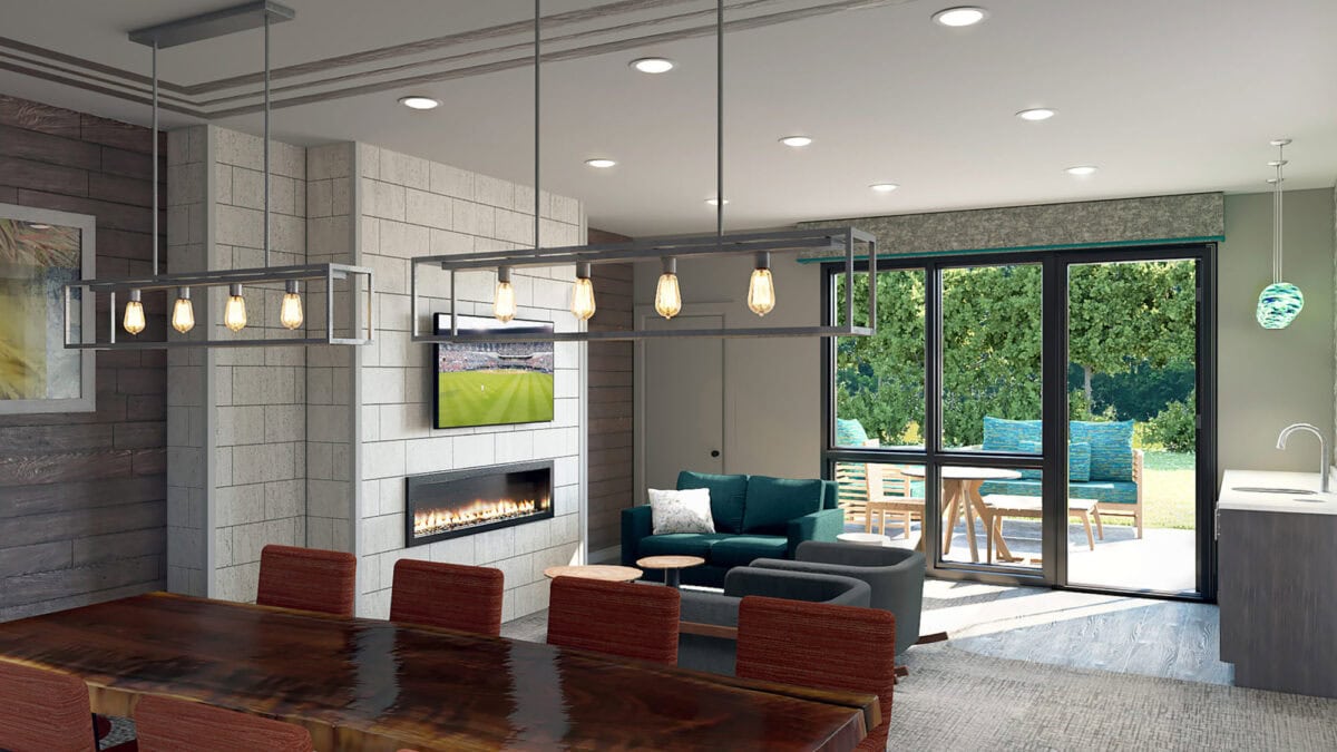 Modern open-plan living room with a dining area, fireplace, wall-mounted TV, and sliding doors leading to a patio with outdoor seating and greenery visible outside.