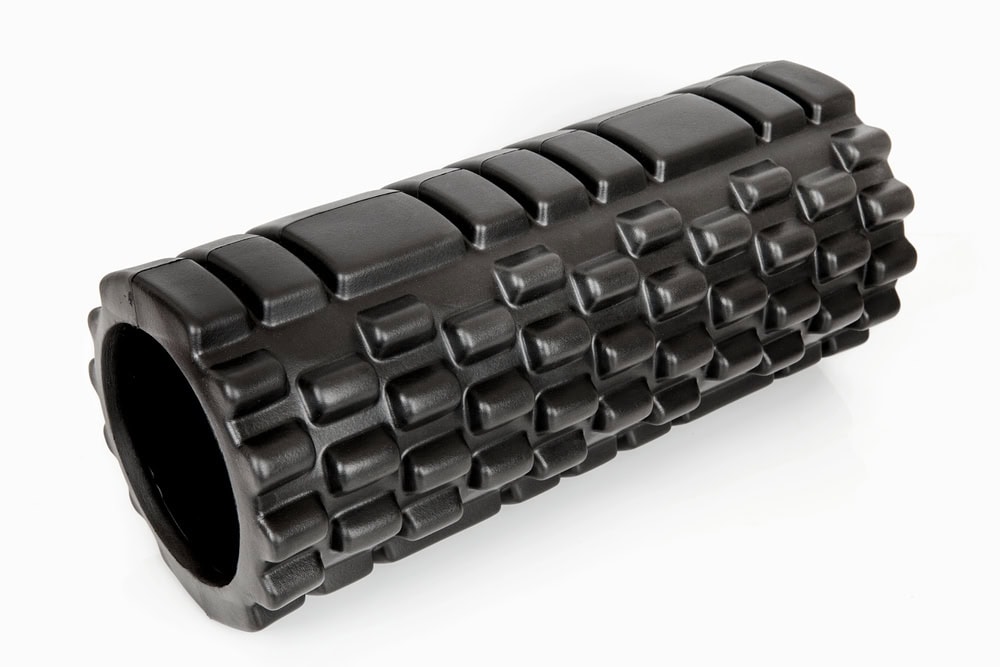 Black textured foam roller with a grid pattern, designed for muscle massage and physical therapy, placed on a white background.