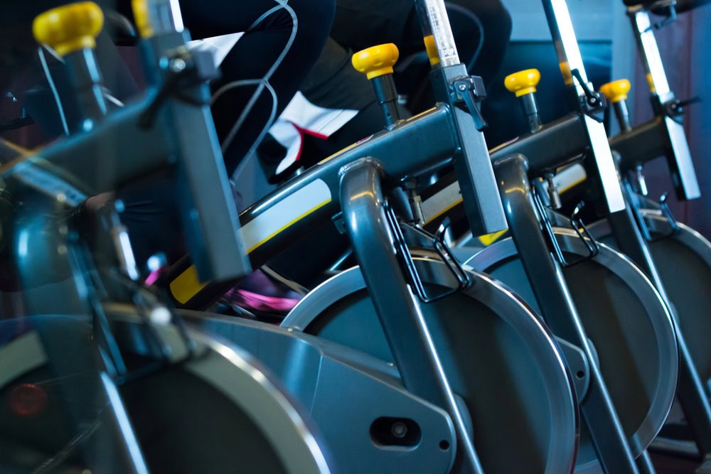 Close-up of people exercising on stationary bikes in a gym, focusing on the pedals and feet in motion.