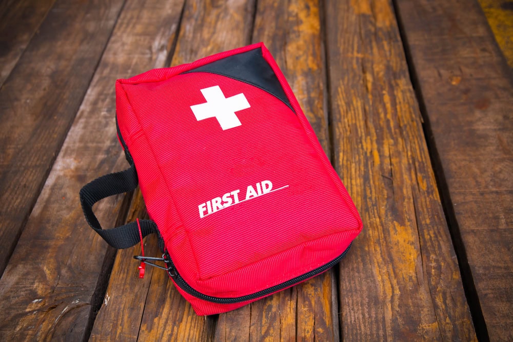 A red first aid kit with a white cross and the text "FIRST AID" on its cover, resting on a wooden surface.