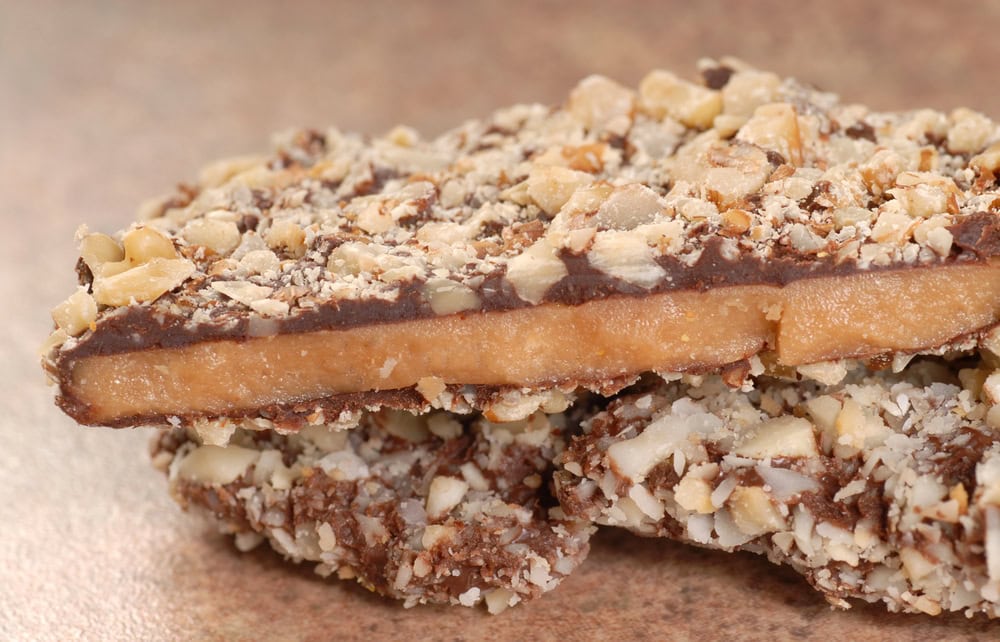Close-up of two pieces of toffee coated with chocolate and chopped nuts, showing the layered texture and crumbly topping.