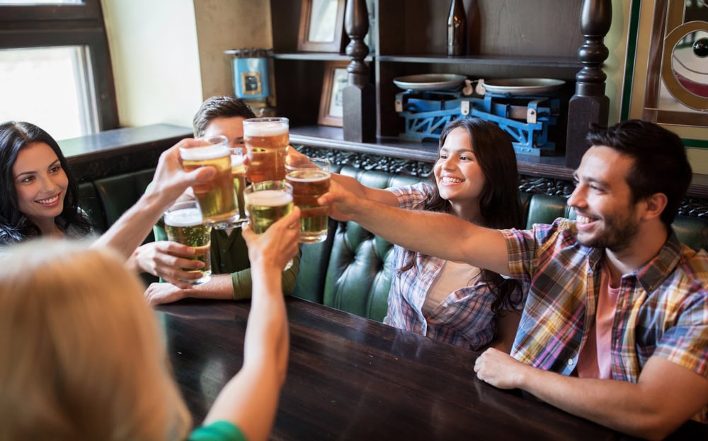 Five people sitting at a pub table, raising glasses of beer together and smiling.