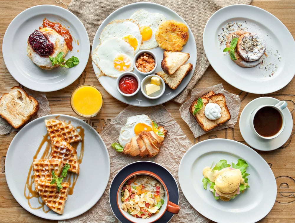 A table set with various breakfast dishes including eggs, waffles, toast, pancakes, beans, juice, and coffee.