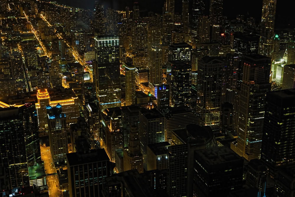 Aerial view of a cityscape at night with illuminated buildings and streets forming a grid pattern.