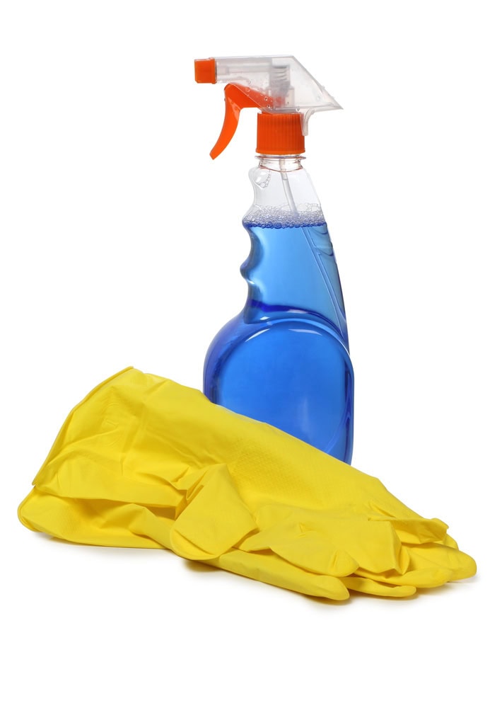 A spray bottle filled with blue liquid and a pair of yellow rubber cleaning gloves on a white background.