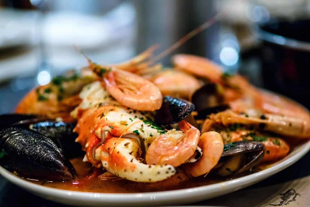 A plate of assorted seafood including shrimp, crab claws, and mussels garnished with herbs, served on a white dish.