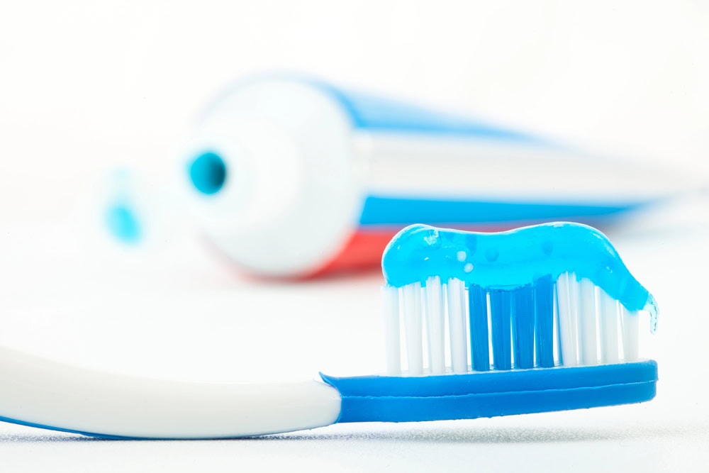 A close-up of a toothbrush with blue and white toothpaste on its bristles, with an open tube of toothpaste in the background.