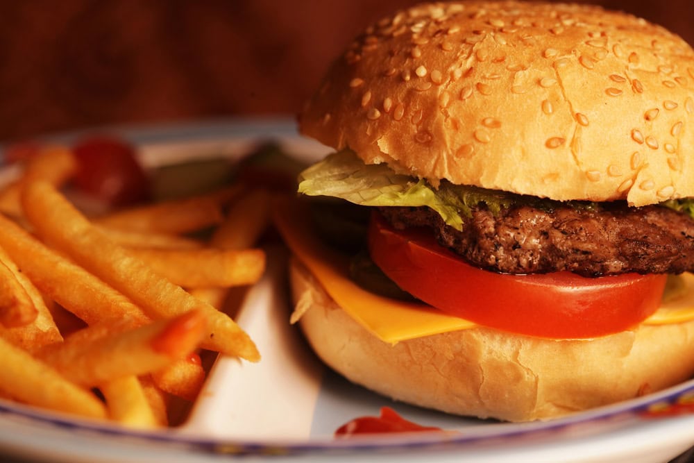 A cheeseburger with lettuce, tomato, and a beef patty on a sesame bun, served with a side of French fries on a plate.