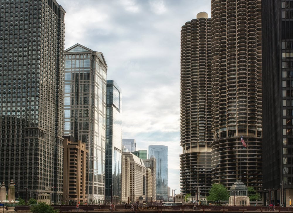 A city scene with modern high-rise buildings, including a pair of round, honeycomb-patterned towers, under a cloudy sky.