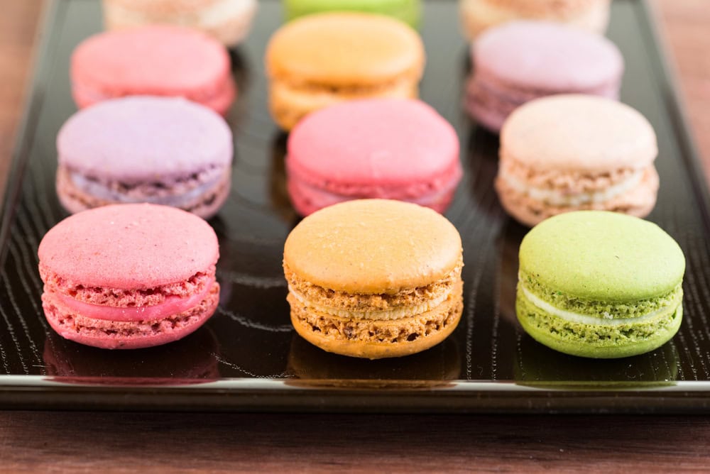 An assortment of colorful macarons arranged in rows on a black tray.