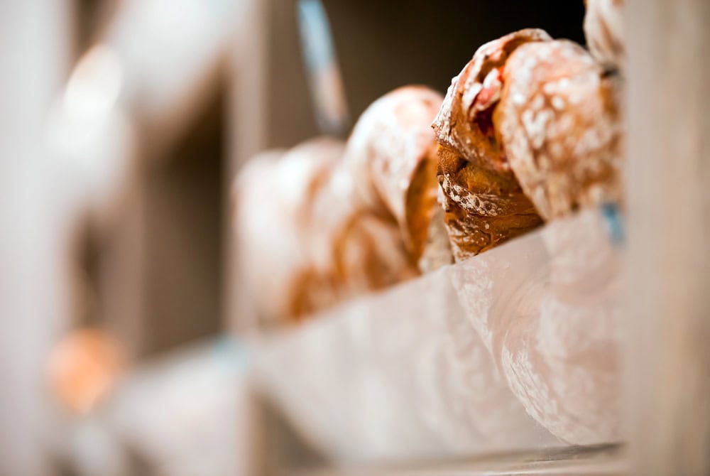 Close-up of several loaves of rustic bread with a dusting of flour, arranged on a bakery shelf.
