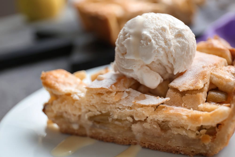 A slice of apple pie topped with a scoop of vanilla ice cream on a white plate.