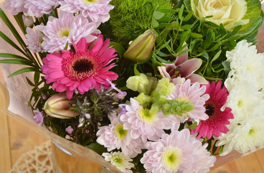 A bouquet of assorted flowers including pink gerbera daisies, white and light purple chrysanthemums, and green foliage.