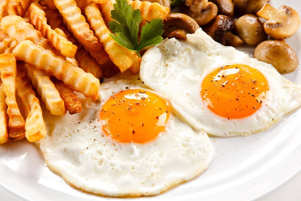 A plate with two sunny side up eggs, crinkle-cut French fries, sautéed mushrooms, and a parsley garnish.