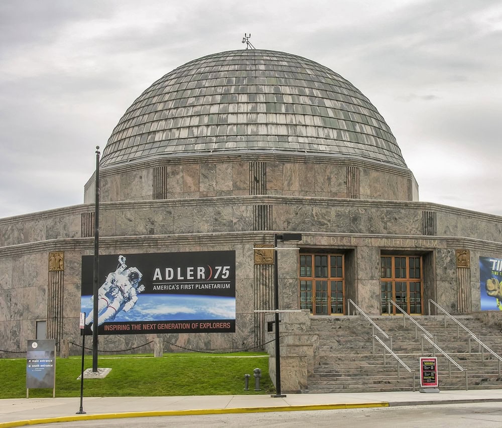 Exterior view of the Adler Planetarium, a domed stone building with banners celebrating its 75th anniversary and promoting space exploration.