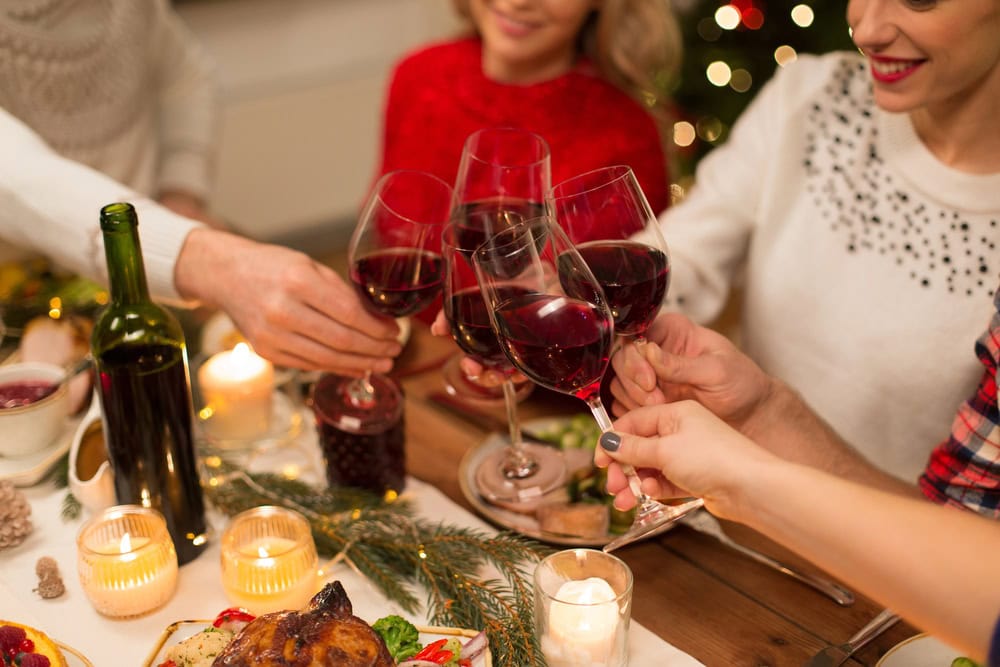 Several people clinking glasses of red wine around a festive, candlelit dinner table with holiday decorations.