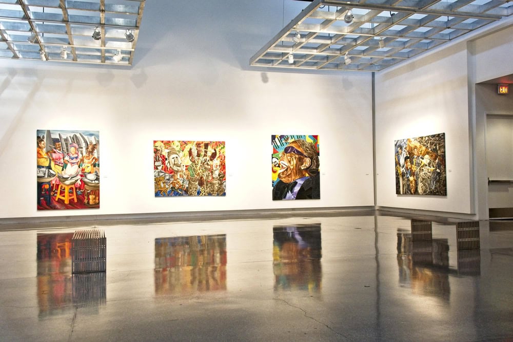Art gallery interior with four colorful paintings displayed on white walls, reflective floor, overhead lighting, and wooden benches placed around the space.