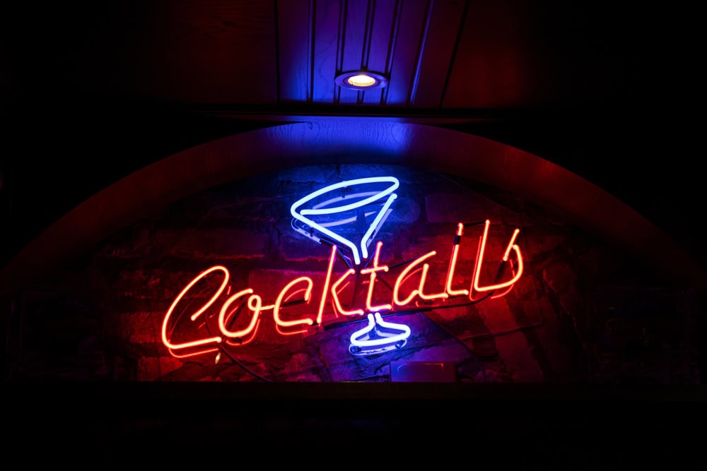 Neon sign displaying the word "Cocktails" in red and a blue martini glass, illuminated against a dark background.