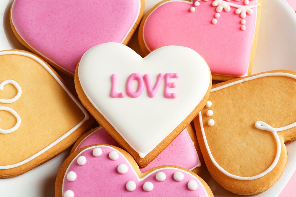 Heart-shaped cookies with pink, white, and yellow icing, including one cookie in the center with "LOVE" written in pink icing.