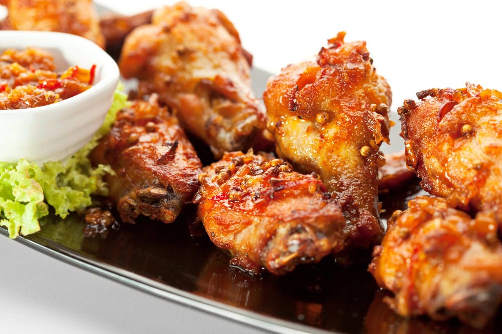 Plate of spicy chicken wings garnished with lettuce, served with a bowl of dipping sauce on the side.