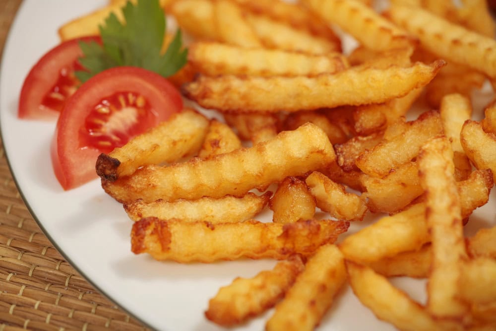 A plate of crinkle-cut French fries garnished with tomato slices and a sprig of parsley.