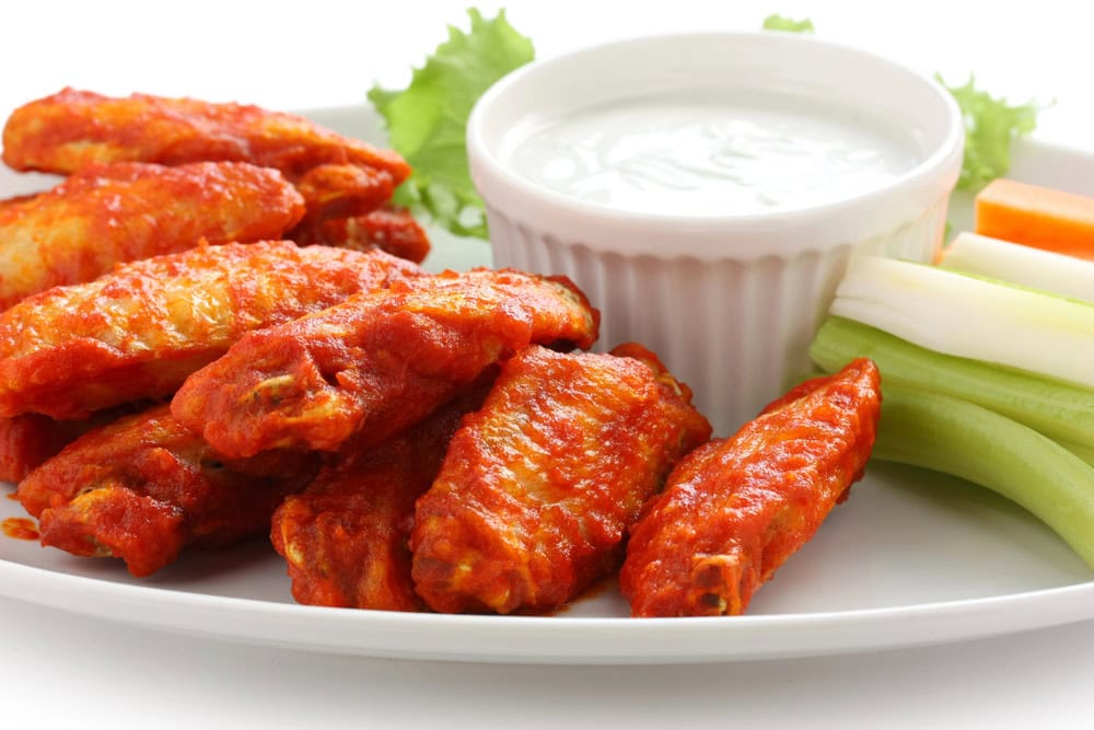 A plate of buffalo chicken wings with celery, carrot sticks, and a cup of ranch or blue cheese dressing.