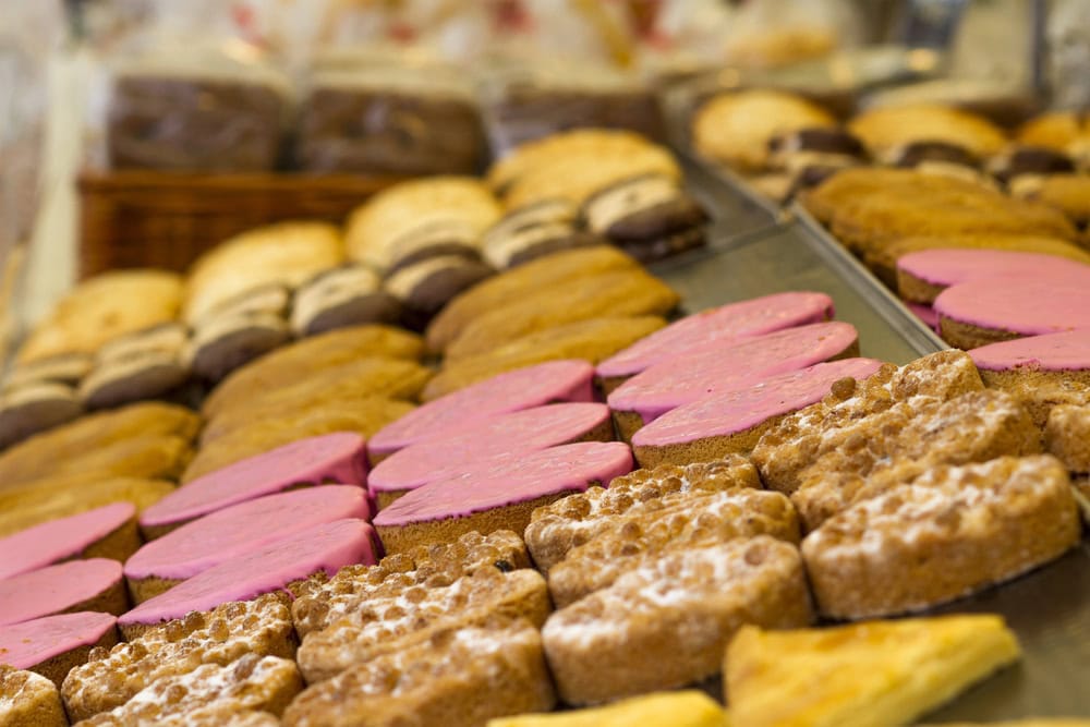 Rows of assorted pastries on display, including heart-shaped cookies with pink icing and rectangular pastries dusted with powdered sugar.