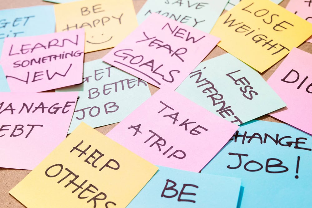 Multiple colorful sticky notes with handwritten resolutions such as "learn something new," "new year goals," "take a trip," "help others," and "less internet" arranged on a surface.