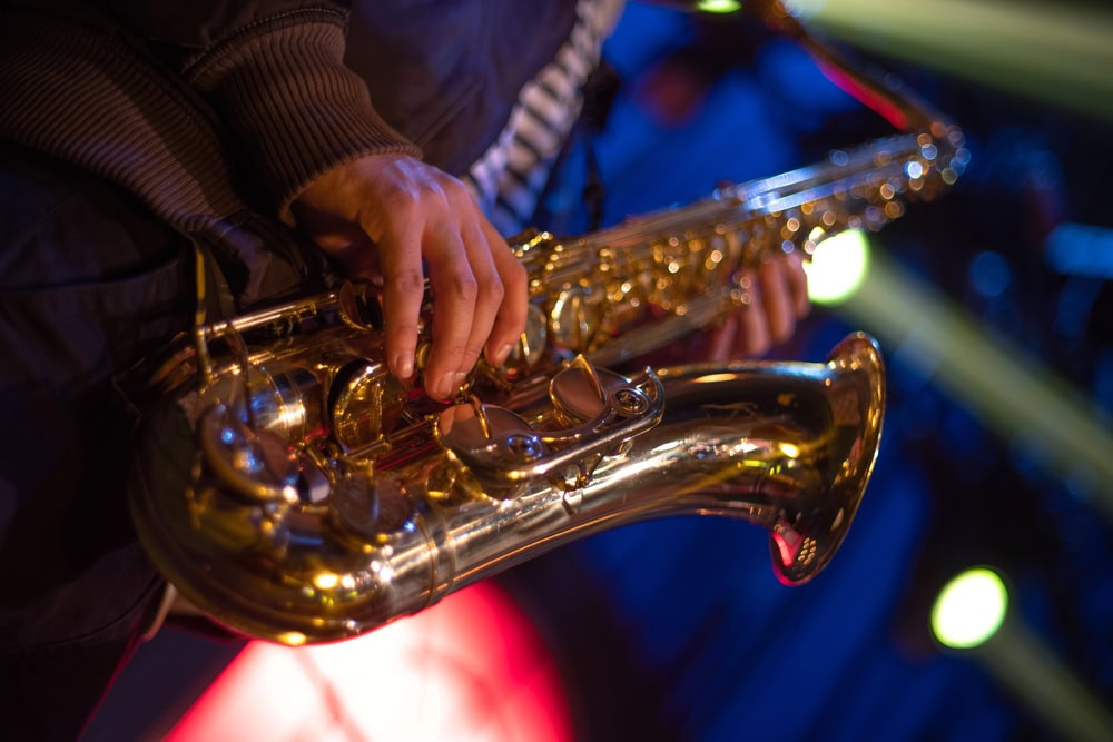 Close-up of a person playing a saxophone on stage, with colorful blurred lights in the background.