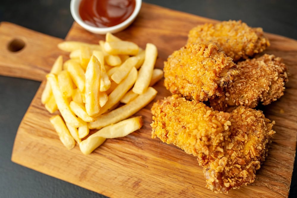 Crispy fried chicken strips and French fries served on a wooden board with a small bowl of dipping sauce.
