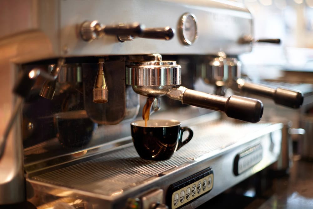 A close-up of an espresso machine brewing coffee into a black ceramic cup placed on the drip tray.