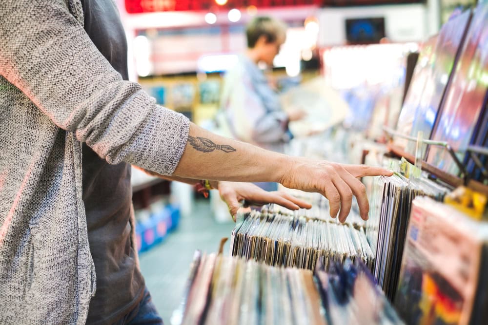 A person browses through vinyl records in a store, with another person visible in the background also looking at records.