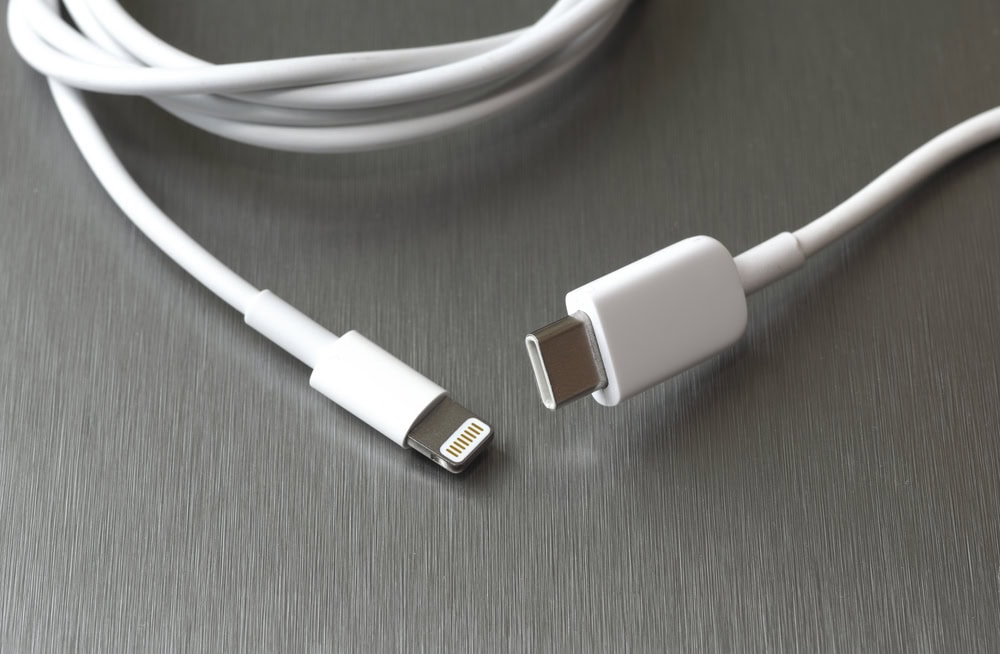 A white cable with a Lightning connector on one end and a USB-C connector on the other, displayed on a metallic surface.