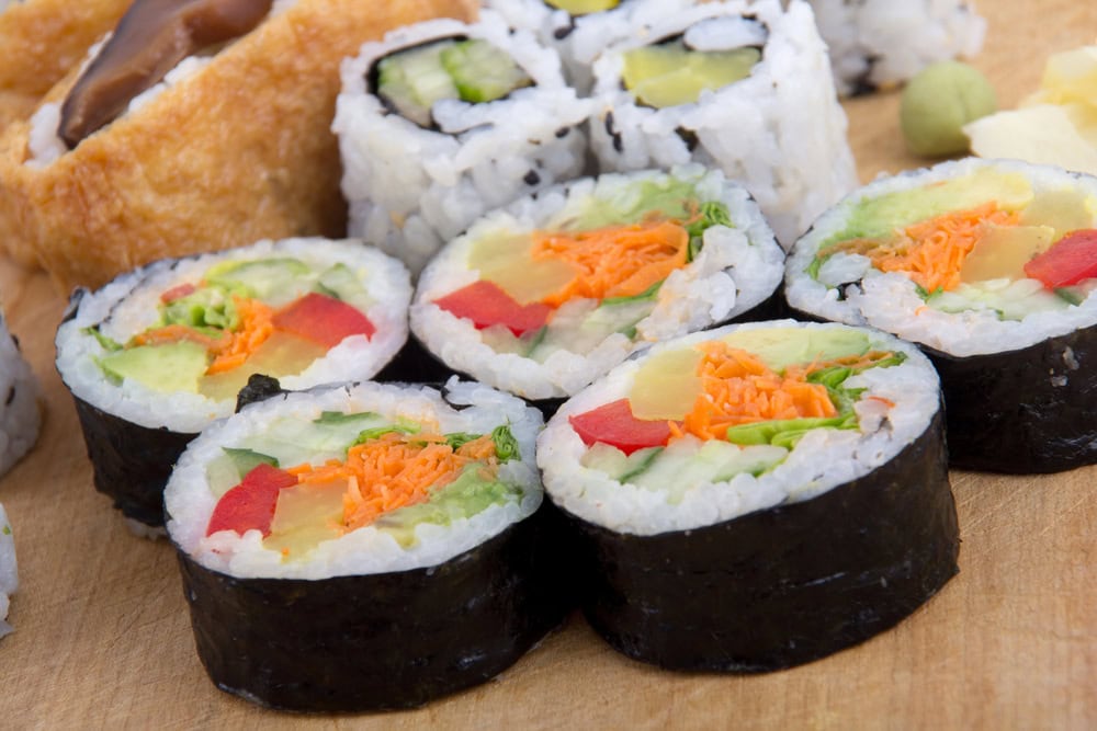 Close-up of assorted vegetable sushi rolls on a wooden surface, with visible ingredients like cucumber, carrot, and avocado.