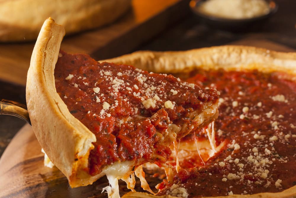 A slice of Chicago-style deep-dish pizza with tomato sauce and melted cheese being lifted from the whole pie.