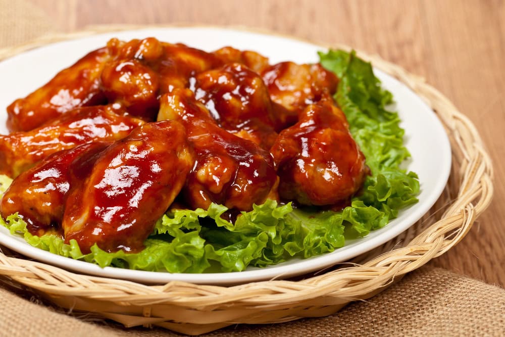 A plate of glazed barbecue chicken wings served on a bed of green lettuce leaves, placed on a woven basket tray.