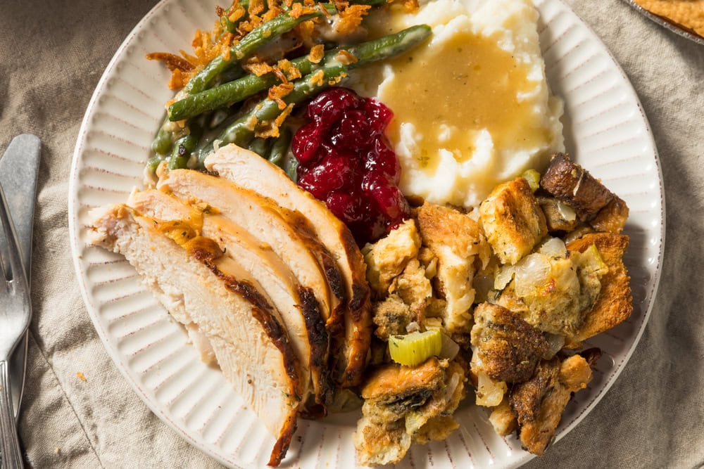 A plate with sliced turkey, stuffing, mashed potatoes with gravy, cranberry sauce, and green beans with fried onions.