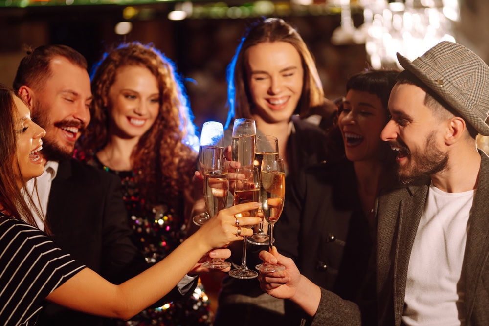 A group of six people standing close together, smiling and raising champagne glasses in a celebratory toast.