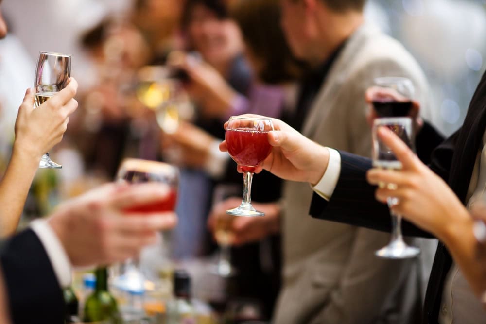 People holding various glasses of wine and cocktails, gathered together and toasting at a social event.