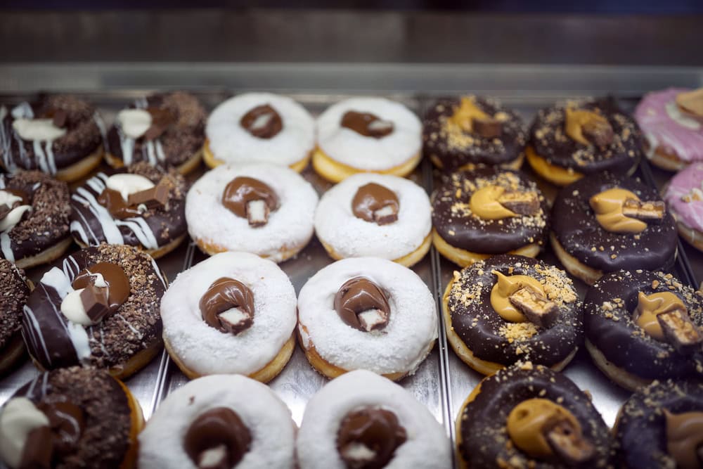A display case filled with assorted decorated donuts, including ones with chocolate, powdered sugar, and various toppings.